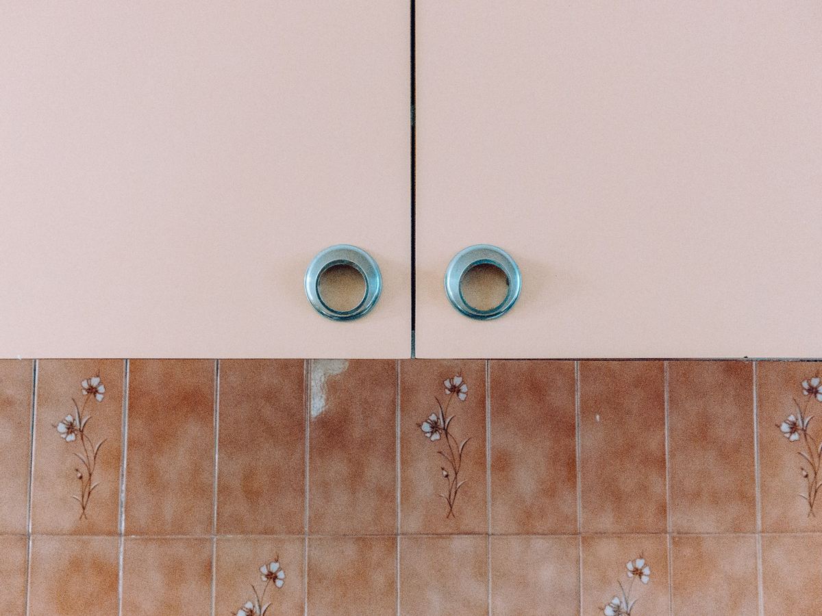 A dated cupboard front with worn laminate and old tiled splashback.