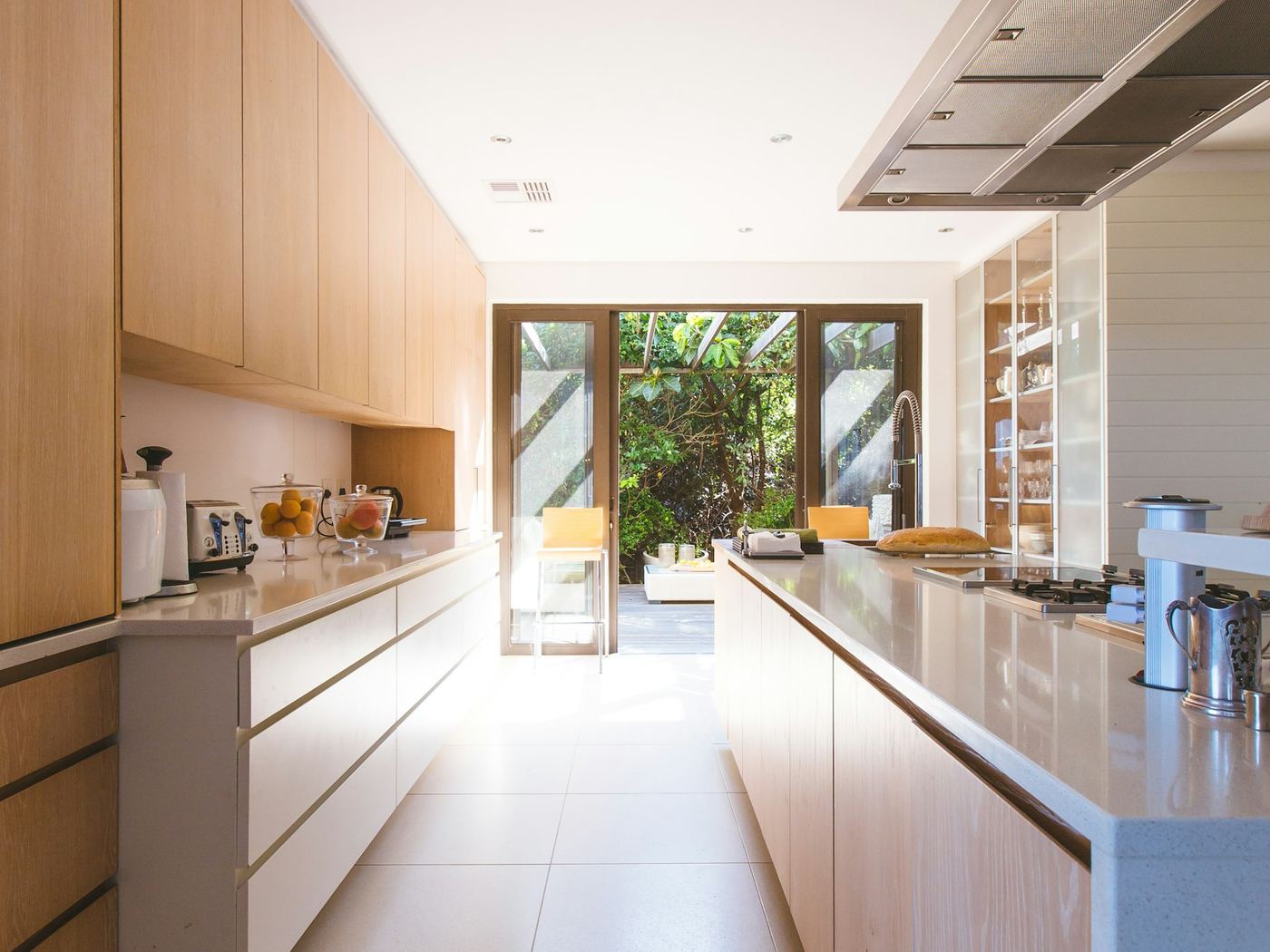 A long galley kitchen with pale handleless cabinetry running to a garden door.
