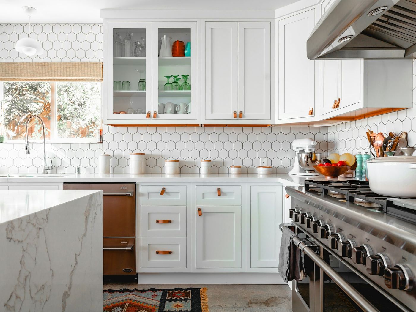 A white kitchen with glass fronted upper cabinets and a stone benchtop.